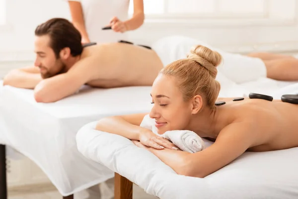 Cônjuges desfrutando de massagem exótica com pedras quentes deitadas no spa — Fotografia de Stock