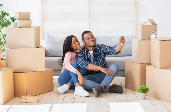 Retrato de comprimento total de belo casal preto tomando selfie no chão no dia em movimento, cercado por caixas de papelão — Fotografia de Stock