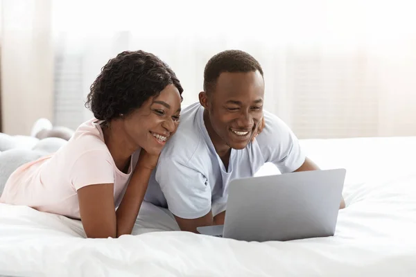 Liebevolle schwarze Mann und Frau mit Laptop im Bett — Stockfoto
