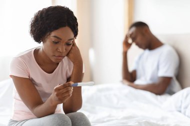 Depressed black woman holding pregnancy test, unintended pregnancy concept clipart