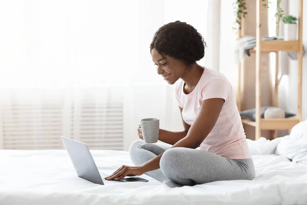 Mujer feliz con taza de té usando el ordenador portátil en la cama — Foto de Stock