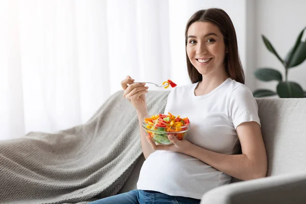 妊娠中の健康的な栄養.幸せな妊婦さんがソファに座り、サラダを楽しむ — ストック写真