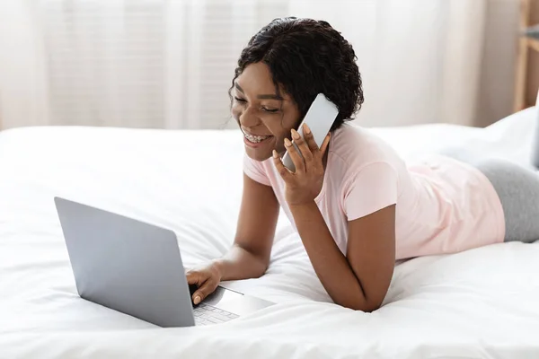 Улыбающаяся американка из Африки разговаривает по телефону и пользуется ноутбуком — стоковое фото