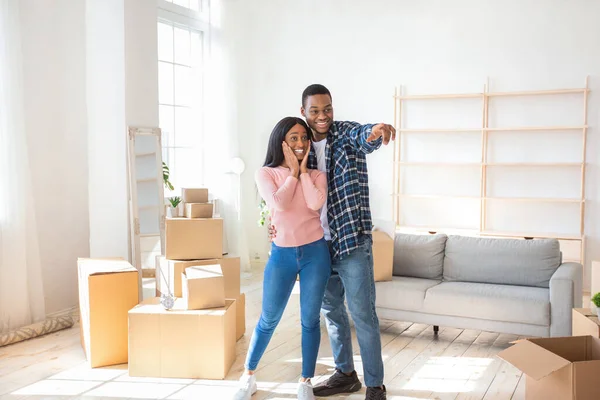 Happy black guy hugging his excited girlfriend, dreaming about furniture placement, pointing somewhere in new house — Stock Photo, Image