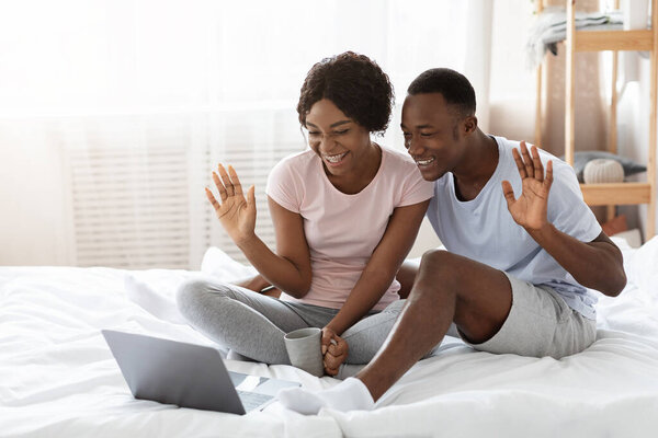Cheerful black couple having online party, using laptop