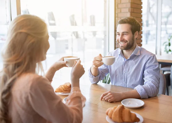 Joven alegre tomando café junto con su novia en la cafetería, charlando y sonriendo durante el desayuno — Foto de Stock