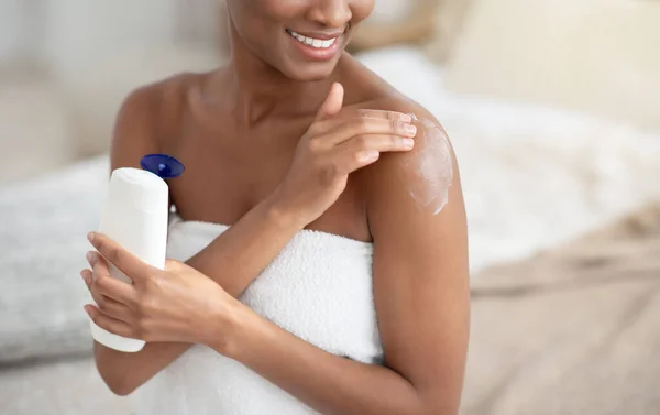 Happy teen african american woman in white handuk after shower applies cream to body — Stok Foto