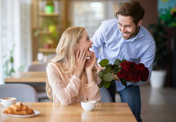 庆祝特殊的时刻。浪漫的小伙子在咖啡馆里送给他兴奋的女朋友一束红玫瑰 — 图库照片