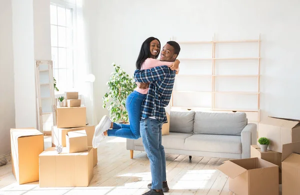 Feliz dia de mudança. Amoroso homem negro abraçando e levantando sua linda namorada em sua nova casa, panorama — Fotografia de Stock