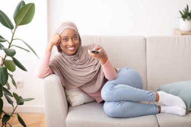 Mutlu siyah kadın tesettürde televizyon seyrediyor. Evdeki rahat koltukta, boş bir yerde.
