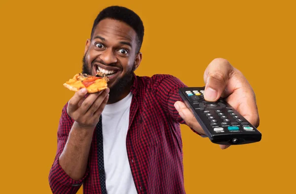 Afro-americano excitado cara comendo pizza assistindo TV, fundo amarelo — Fotografia de Stock