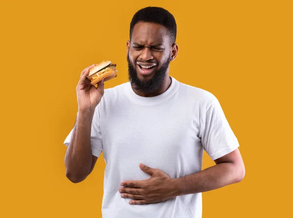 Homem negro sofrendo de dor de estômago após o hambúrguer sobre fundo amarelo — Fotografia de Stock