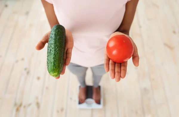 Vue ci-dessus de dame afro-américaine tenant tomate et concombre, debout sur des échelles, choisissant une alimentation saine, gros plan — Photo