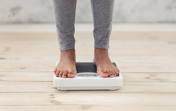 Closeup of young African American woman standing on scales indoors, checking her weight, cropped view of feet — Stock Photo, Image