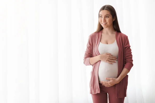 Anyasági koncepció. Portré mosolygó terhes Millennial Woman álló ablak mellett — Stock Fotó