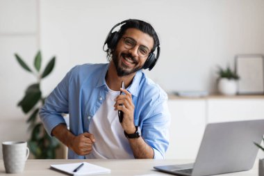 Kablosuz kulaklıklı neşeli bir Arap adam. Akıllı telefondan müzik dinliyor ve şarkı söylüyor.