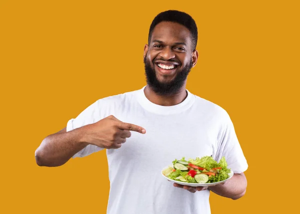 Homem Africano apontando o dedo na salada em pé sobre fundo amarelo — Fotografia de Stock