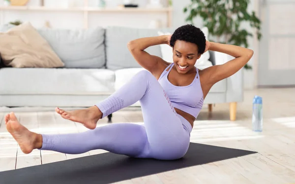 Sport tijdens de afsluiting. Mooie zwarte dame doet thuis fitness op yoga mat, het trainen van haar hele lichaam — Stockfoto