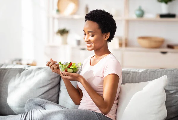 Koncepcja zrównoważonego odżywiania. piękny czarny lady jedzenie pyszne warzywa sałatka na przytulny kanapa w domu — Zdjęcie stockowe