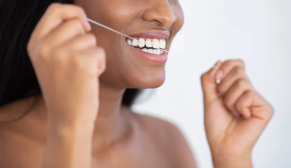 Cantik tersenyum african american perempuan memegang benang gigi, membersihkan gigi, menghapus makanan antara gigi — Stok Foto