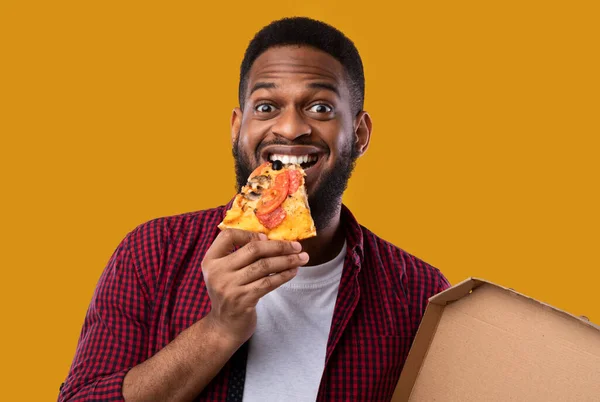 Homem afro-americano comer pizza fatia de pé sobre fundo amarelo — Fotografia de Stock