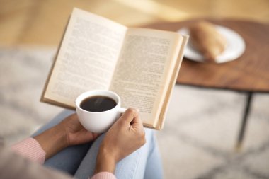 Kahve kitabı okuyan tanınmayan siyahi kadın, evde huzurlu bir sabah geçiriyor, boş yer var.