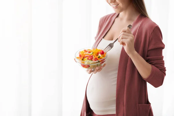 Femme enceinte avec bol de salade de légumes debout près de la fenêtre à la maison — Photo