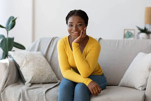 Descanso en casa. Sonriente dama africana relajándose en el sofá en la sala de estar —  Fotos de Stock