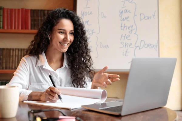 Senhora sentada à mesa, usando computador e escrevendo em caderno — Fotografia de Stock