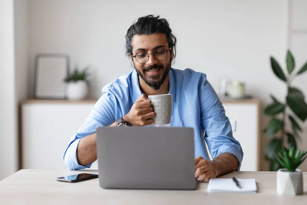 Young Smiling Arab Freelancer Guy Using Laptop And Drinking Coffee At Home — Stock Photo, Image