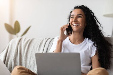Neşeli kadın telefonda konuşuyor ve dizüstü bilgisayar kullanıyor.