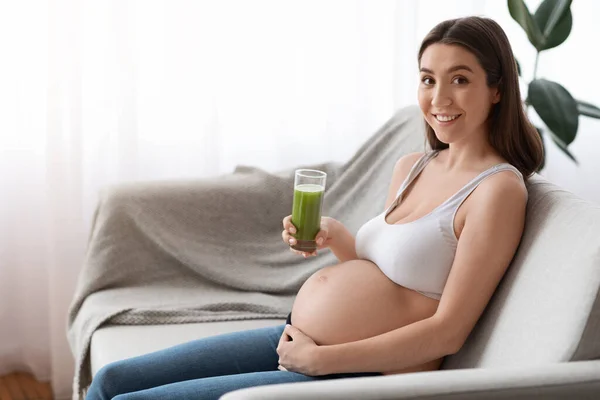 緑のスムージーのガラスと幸せな若い妊娠中の女性はカウチに座って — ストック写真