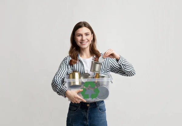 金属リサイクル。錫缶付きプラスチック容器ボックスを持つ若い笑顔の女性 — ストック写真