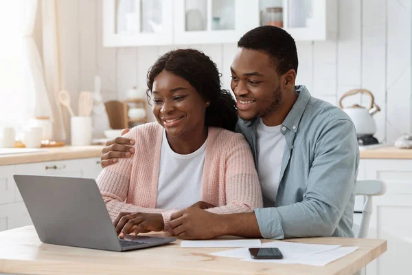 Sorrindo casal preto com laptop na cozinha contas de cálculo, gestão de finanças juntos — Fotografia de Stock