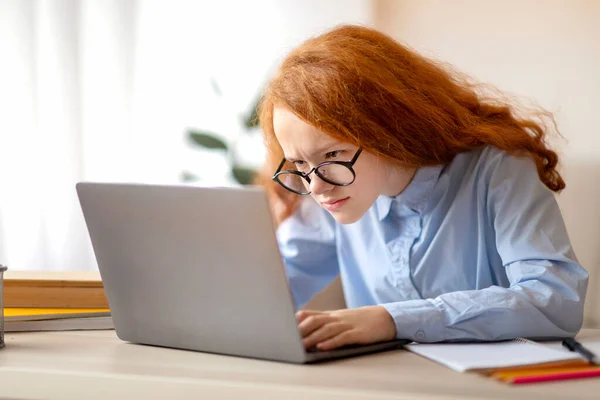 Girl wearing glasses sitting at table, using laptop — Stock Photo, Image