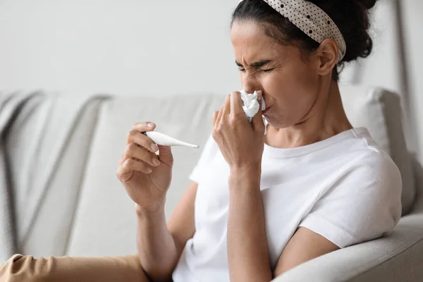 Nahaufnahme einer kranken jungen Frau, die niest und Körpertemperatur misst — Stockfoto