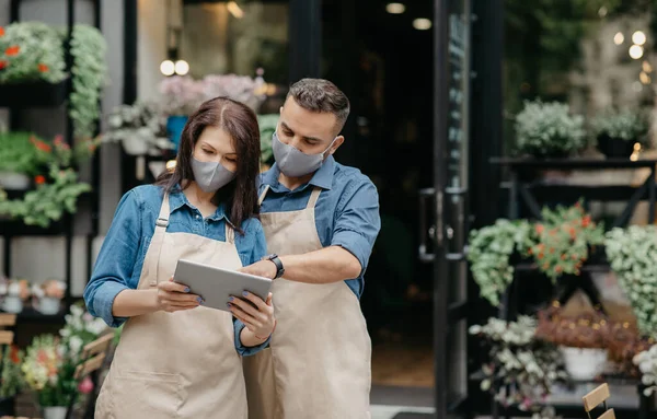 Pessoas, negócios, tecnologia, venda e floricultura. Ocupado jovem masculino e feminino em aventais de trabalho em tablet digital — Fotografia de Stock