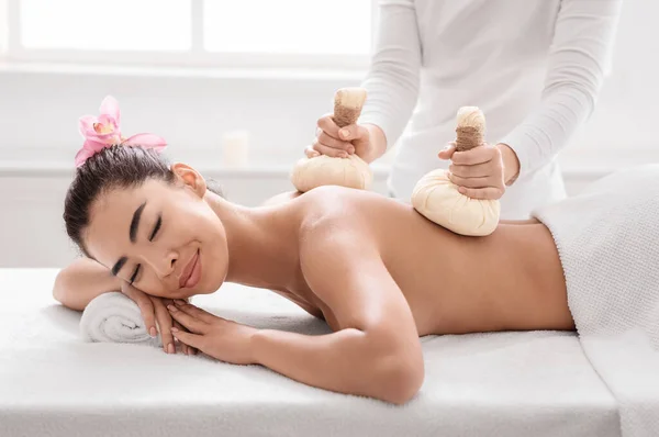 Atraente asiático senhora relaxante no spa center, recebendo massagem com ervas bolas — Fotografia de Stock