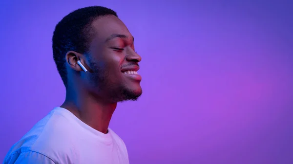 Entspannter Afrikaner hört Musik in drahtlosen Airpods-Kopfhörern in Neonlicht — Stockfoto