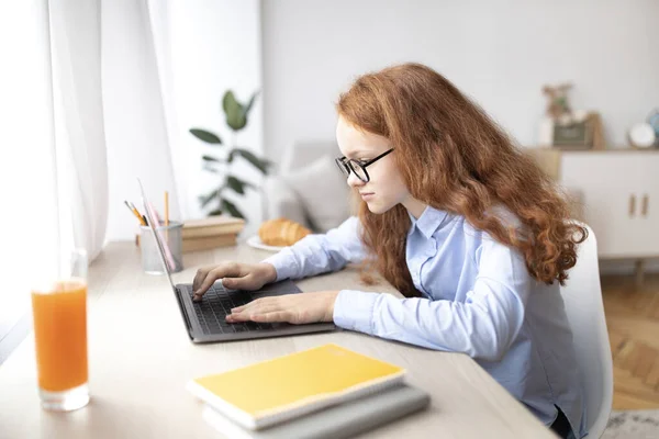 Девушка сидит за столом, использует ноутбук, печатает на клавиатуре — стоковое фото