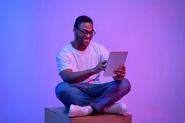 젊은 흑인 프리랜서가 밝은 네온 빛 아래 디지털 태블릿을 들고 앉아 있습니다. — 스톡 사진