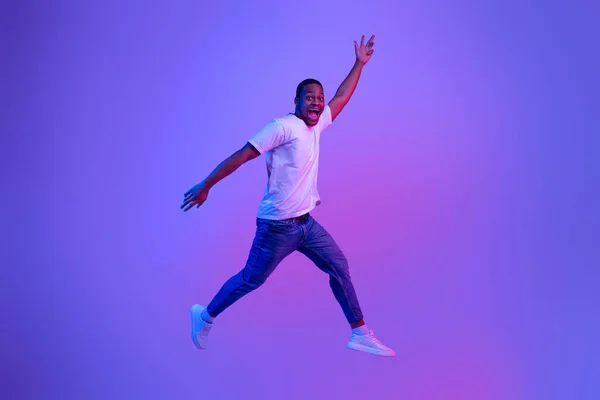Emocionado divertido chico negro saltando en luz de neón sobre fondo púrpura —  Fotos de Stock