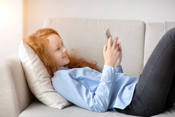 Ragazza che utilizza il suo telefono cellulare appoggiato sul divano — Foto Stock