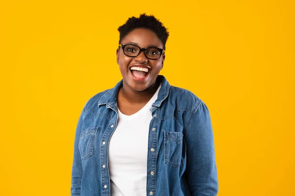 Alegre oversized preto senhora vestindo óculos posando no fundo amarelo — Fotografia de Stock