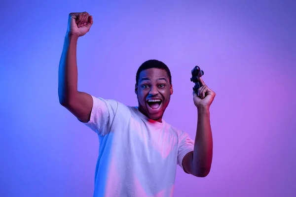Νικητής βιντεοπαιχνιδιών. Ενθουσιασμένος μαύρος που κρατάει χειριστήριο, γιορτάζει την επιτυχία, νέον φως — Φωτογραφία Αρχείου