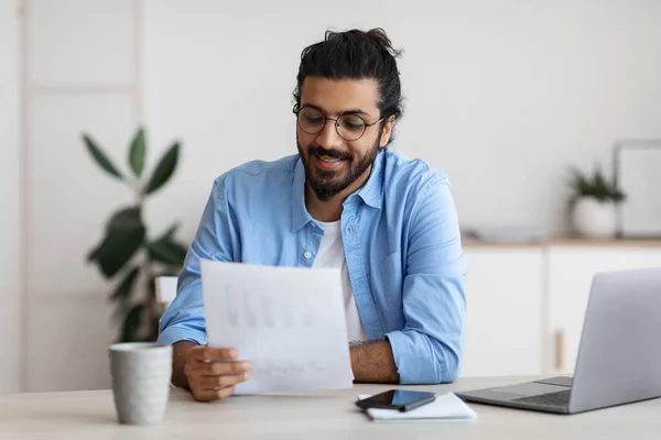 Junge arabische männliche Selbstunternehmerin arbeitet mit Papieren am Schreibtisch im Home Office — Stockfoto