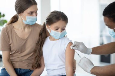 Maskeli ebeveyn ve çocuk Coronavirus aşısı oluyor, doktor klinikte covid-19 aşısı yapıyor.