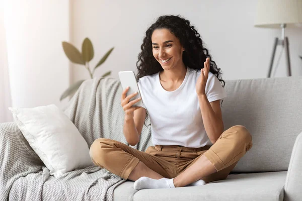 Mujer joven positiva sentada en el sofá, teniendo llamada en línea — Foto de Stock