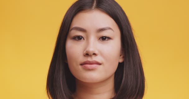 주황색 배경으로 카메라를 보고 있는 매력적 인 동양 여성의 스튜디오 사진 — 비디오