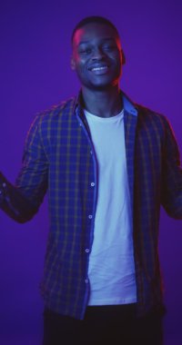 Genç Afrikalı Amerikalı adam arka planda neon ışıklarla dans ediyor, eğleniyor, dikey hikaye videosu çekiyor.
